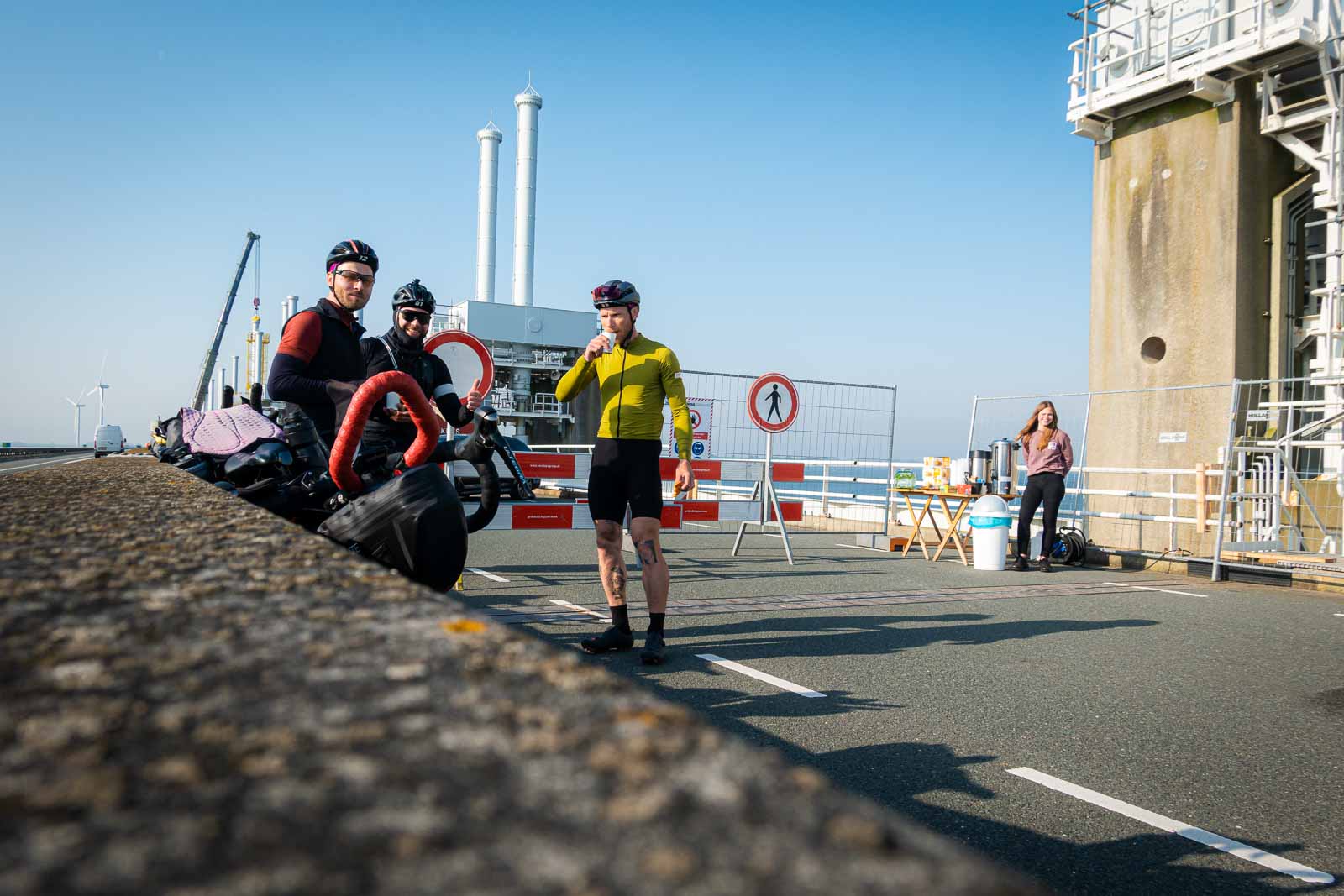Drie fietsers wachten op een bouwplaats van een brug, drinken koffie en eten koekjes
