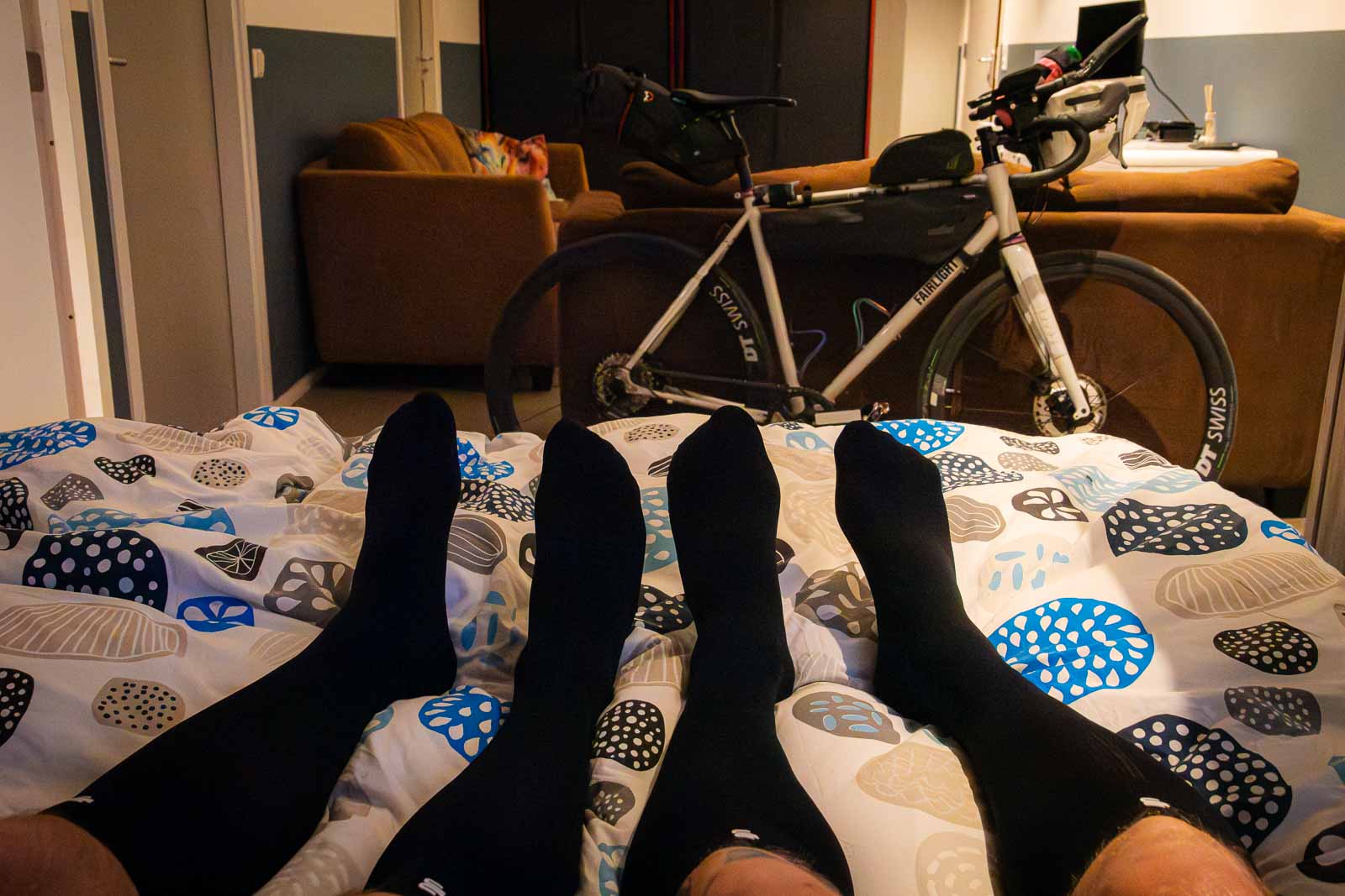 Twee deelnemers van Race rond Nederland liggen in bed met herstelsokken aan na een vermoeiende dag.
