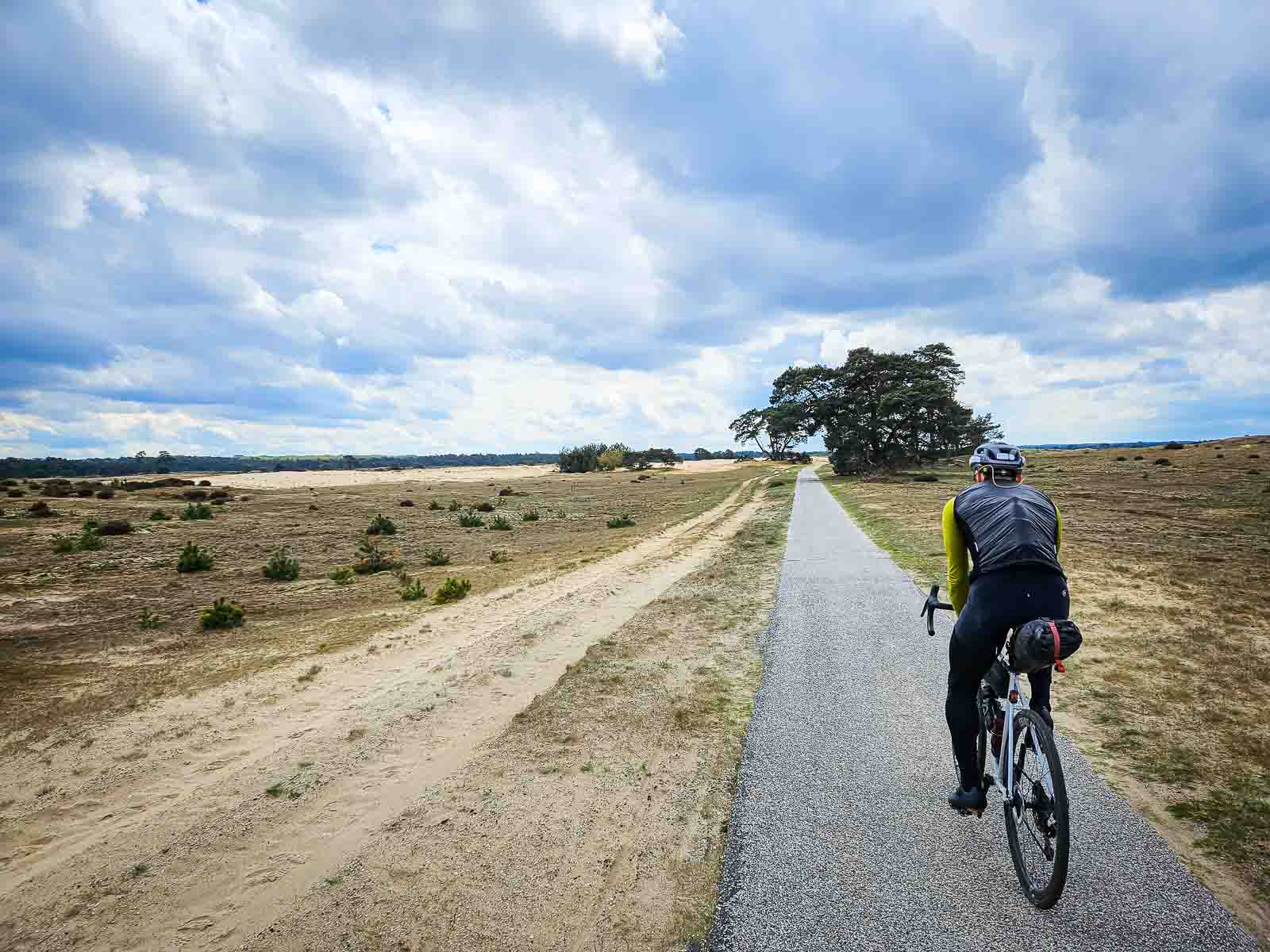 Een fietser rijdt over een lange rechte weg door een prachtig heidelandschap.