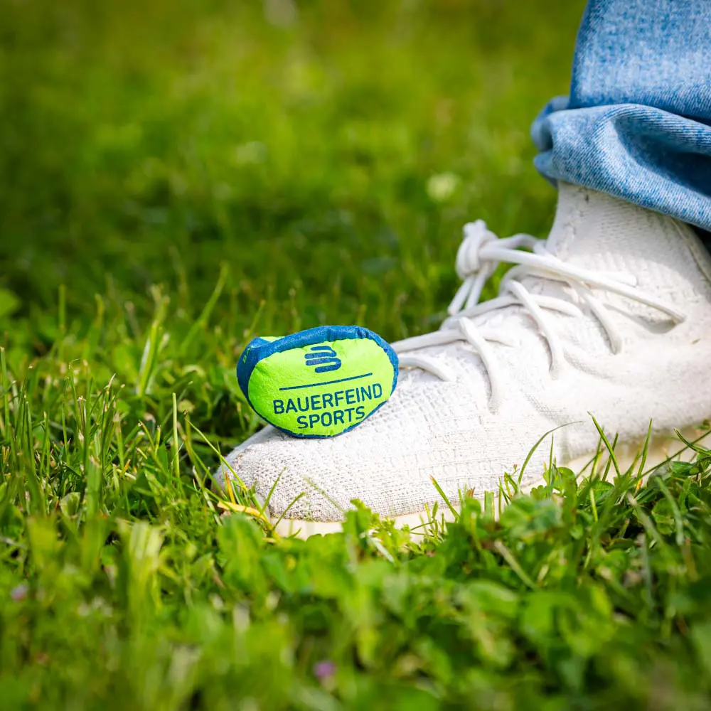 Kleine Bauerfeind Sports bal op gras, geplaatst naast een witte schoen.