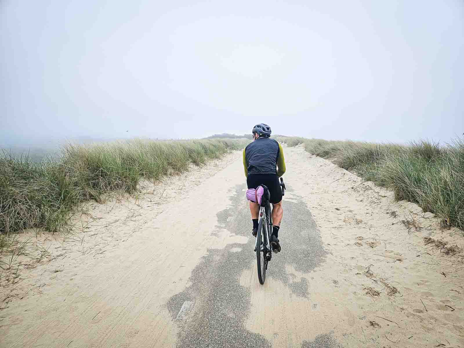 Een fietser rijdt over een prachtige duinweg die gedeeltelijk bedekt is met zand.